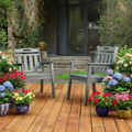 Two gray garden chairs on  a stone building and plants in the background.
